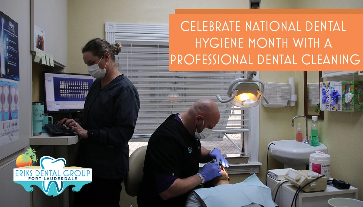 dnetist cleaning a patient's teeth while assistant works on the computer in the background