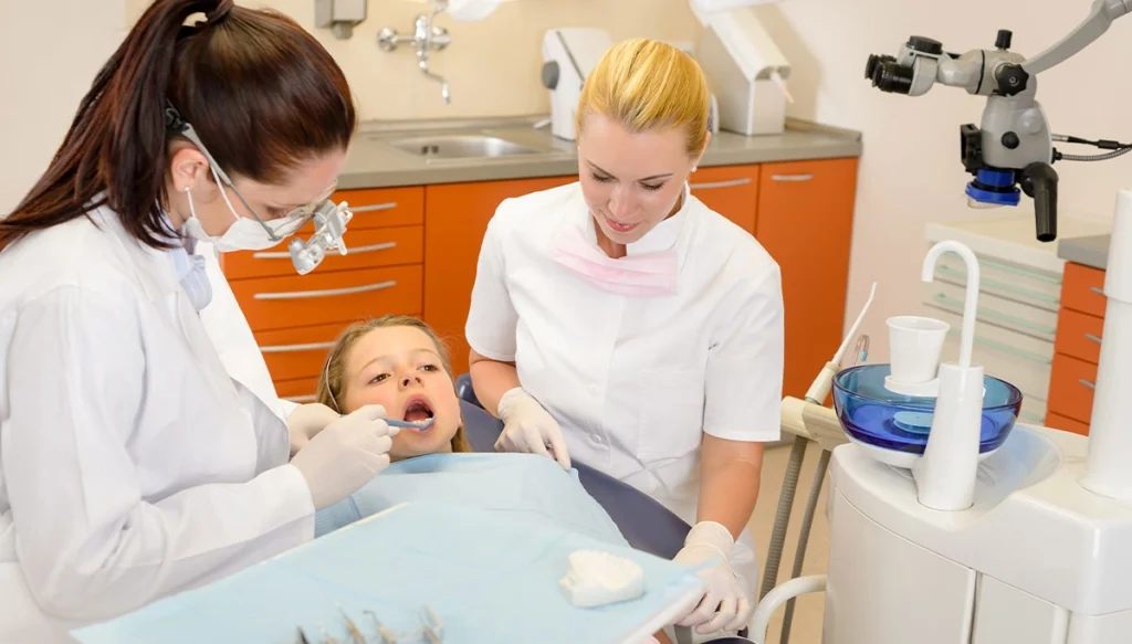 dentist examines little girl's teeth while the assistant observes
