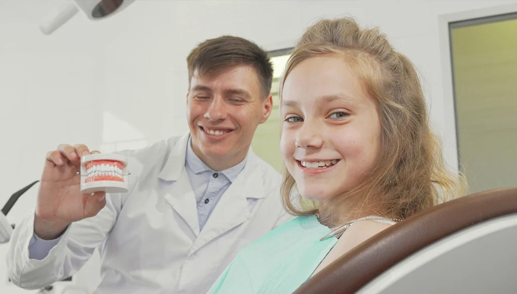 Young girl and dentist smiling while the dentist is holding a pair of dentures
